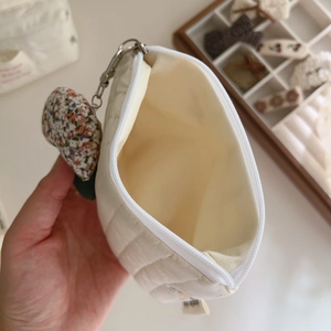 Close-up of beige quilted makeup bag with zipper and floral heart charm attachment