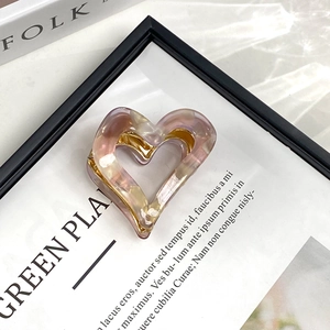Detail of pink marble acetate heart claw clip with gold metal grip on a vintage book