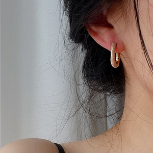 Close-up of minimalist U-shape gold hoop earring with beige enamel on female model