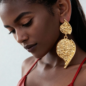 Detailed close-up of golden wrinkled heart earrings worn by a model for a stylish look