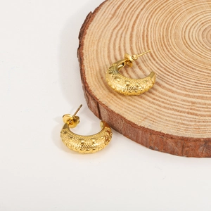 Close-up of gold hoop earrings with embossed heart patterns on a wood slice