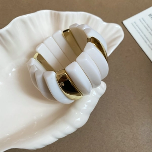 Detailed view of broad acrylic bangle in white and gold on shell tray