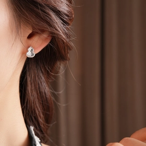 Detailed view of silver gourd shaped earring with irregular hollowed metal texture on ear