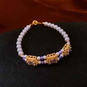Detail of pearl bracelet with purple square zircons and golden vintage charms