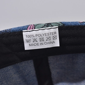 Detail of the 100% polyester washing label on the blue denim-style baseball cap