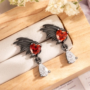 Gothic black angel wing stud earrings with red heart and clear teardrop gems on wood