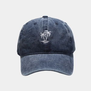 Close-up of white palm tree embroidery on navy blue washed denim baseball cap surface