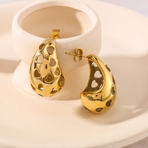 Goldene hohle Tropfenohrringe mit Herzmustern auf einem minimalistischen Schmuckständer
