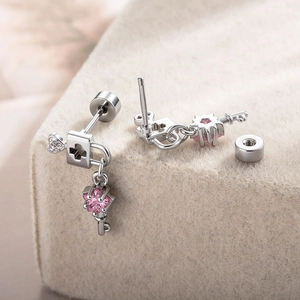 Silver lock and key earrings with pink gems and cross pendants on beige felt
