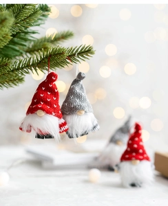 Close-up of handmade felt Christmas gnomes hanging on a tree with festive bokeh lights