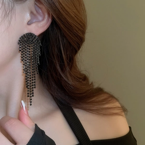 Detail view of long black tassel earrings with sparkling rhinestones on model's ear