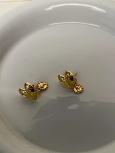 Detail of gold heart earrings with dangling coin charms on a minimalist ceramic plate