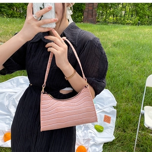 Pink crocodile-embossed underarm bag shown in a sunny outdoor picnic setting