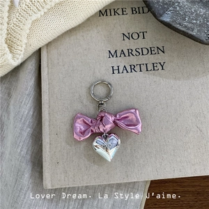 Close-up of pink bow and silver heart pendant keychain on minimalist fabric background