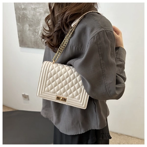 Detailed view of beige quilted handbag with gold chain strap worn by a female model