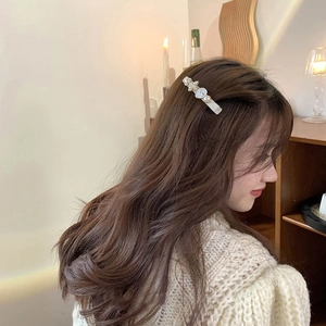 Elegant gold hair clip with white pearls and clover design worn by a model in soft light
