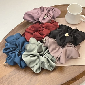 Detail of silk satin scrunchies in Morandi colors with golden metal charms on a tray