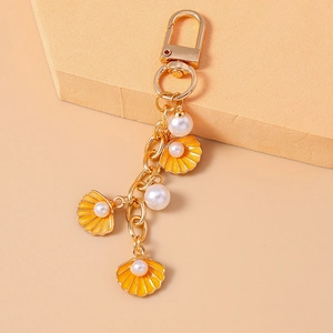 Detail of golden keychain with three orange shells and white pearls on warm background