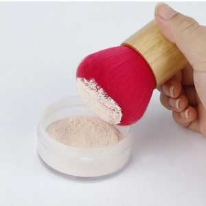 Detail of bamboo handle brush with red bristles picking up fine makeup powder