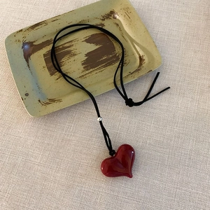 Macro detail of red heart glass pendant on black velvet cord over rustic ceramic plate