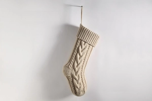 Close-up of a large beige knitted Christmas stocking hanging on a clean white wall