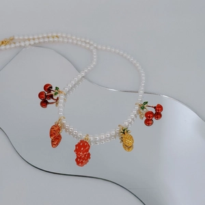 Detailed view of a double-strand pearl necklace with cute strawberry and pineapple charms
