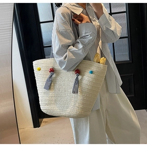 Detail of hand-woven straw tote bag with colorful poms and striped tassel trim