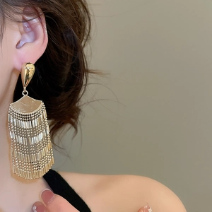 Close-up of golden fan-shaped tassel earrings on model showing metal plating details