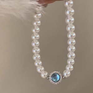 Detailed macro of a pearl necklace featuring a round blue gemstone pendant with silver settings