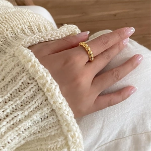 Golden beaded stackable ring worn by a model against a warm knit sweater background