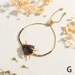 Detail of adjustable gold beetle bracelet featuring colorful gemstone inlay on white background