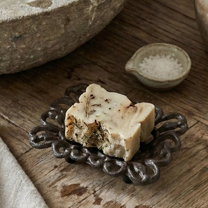 Rustic cast iron hollow soap dish with handmade herbal soap on a wooden table