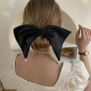Detail of a large black satin bow hair clip with elegant hanging pearl accents