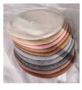 Close-up of stacked wool beret hats in various autumn colors on white fabric