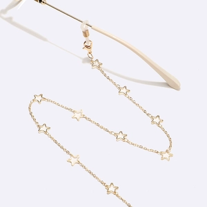 Close-up of golden glasses chain with white enamel star pendants on thin metal link