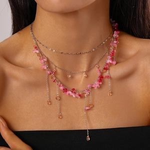 Detail of layered silver necklace with pink resin flowers and amber waterdrop pendant