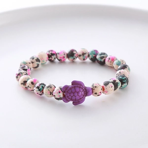 Detail of colorful speckled beads bracelet with a purple sea turtle charm on a white plate
