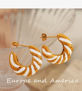 Close-up of gold and white twisted C-shaped titanium steel earrings on a soft background