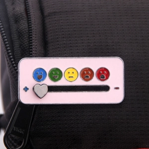 Macro detail of a pink enamel mood slider pin showing emoji emotions on black fabric