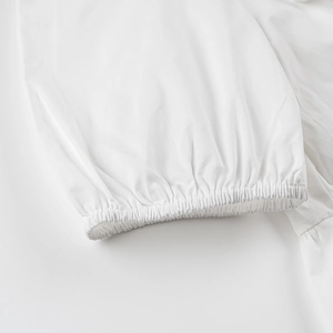 Détail des poignets plissés élastiques sur un chemisier blanc en coton à manches bouffantes