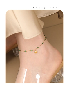Detail of gold ankle bracelet with green beads and a shell pendant on a model ankle