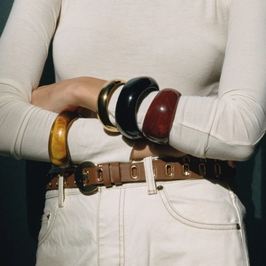 Dettaglio di bracciali in resina impilati in ambra, marmo e finiture in metallo dorato