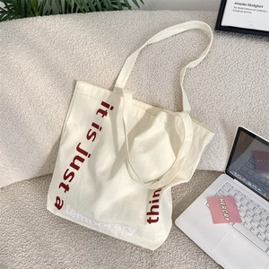 Gros plan du sac fourre-tout en toile crème sur canapé blanc avec imprimé artistique rouge