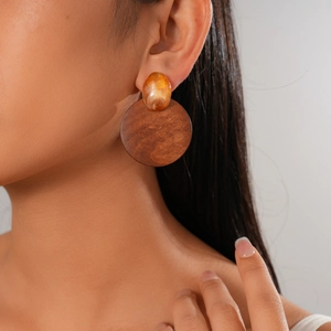 Gros plan de boucles d'oreilles rondes géométriques en résine et bois portées par un mannequin