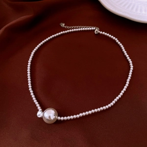 Detailed close-up of a pearl necklace with zircon accents on a dark red satin background