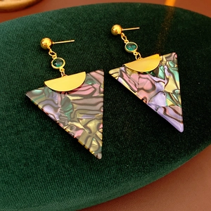Detail of vintage gold triangle earrings with green stone on green velvet background