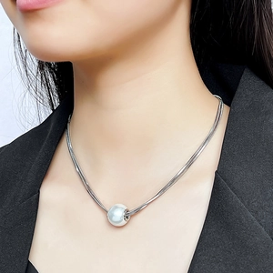 Detail of a minimalist white pearl pendant on a silver snake chain over black fabric