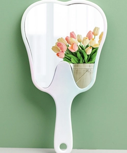 Tooth-shaped white plastic handheld mirror with handle reflecting a vase of tulips