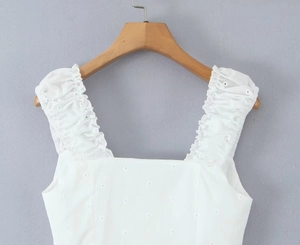 Detail of white cotton top featuring delicate floral embroidery and ruffled straps on a hanger