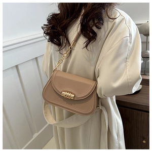Detail of beige saddle bag featuring gold cylindrical clasp and metal chain strap